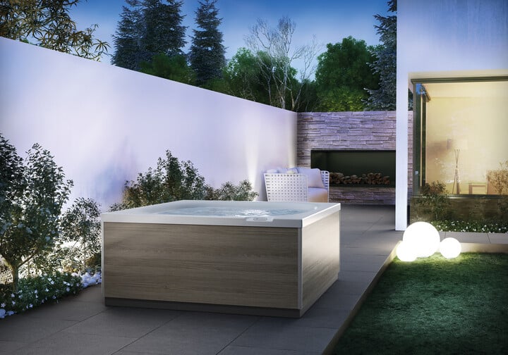 Jacuzzi® da esterno freestanding con pannelli in legno, installata in un patio moderno illuminato di sera.